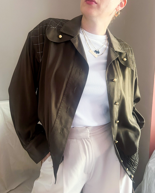 Person wearing a dark green vintage 70s 80s jacket over a white shirt and light-colored pants.