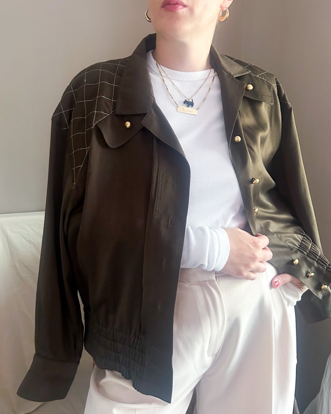 Person wearing a dark green vintage jacket over a white shirt and pants, sitting on a light-colored couch.